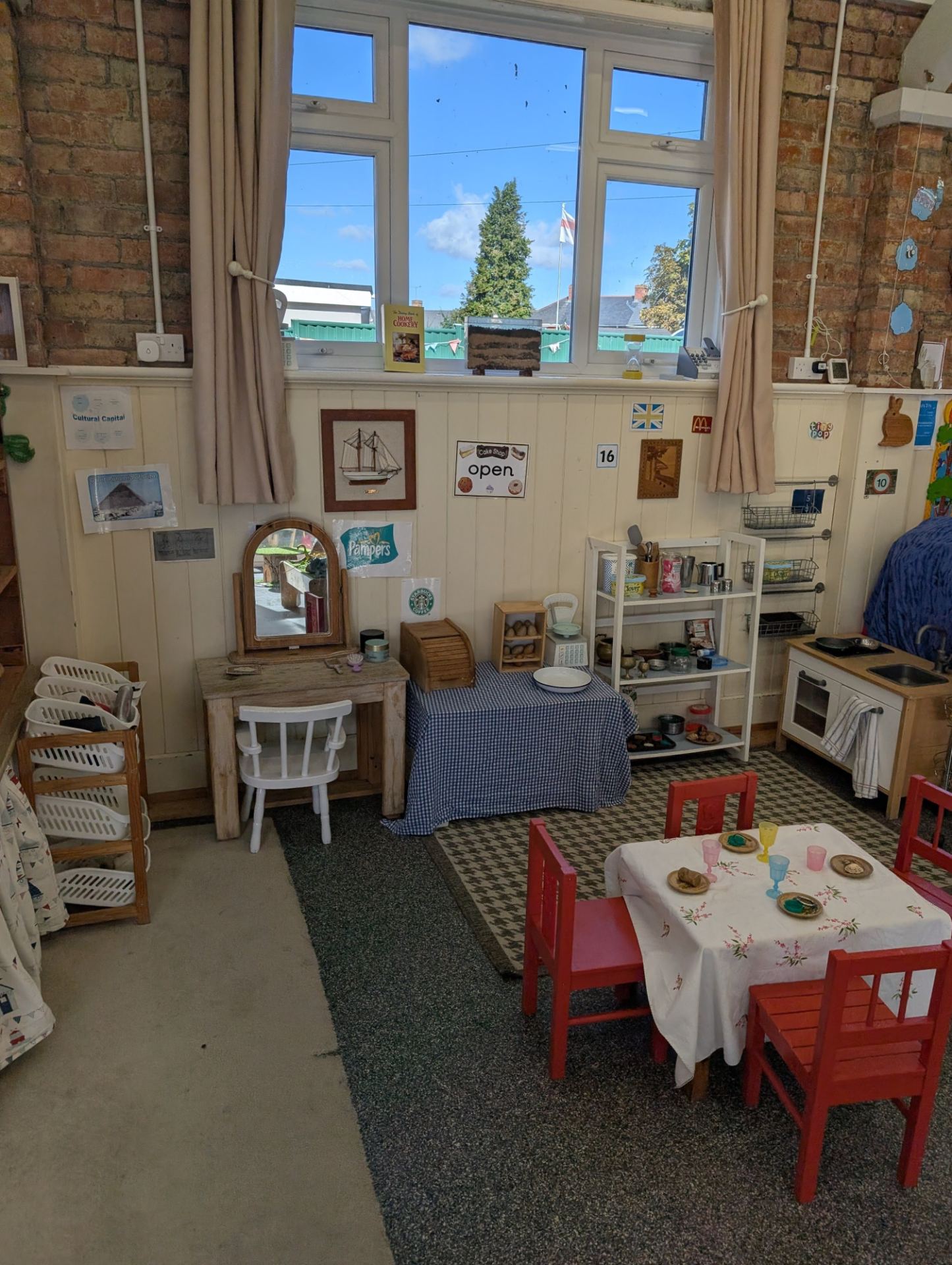 A bright, well-appointed role-play classroom with a domestic kitchen and dining setup.